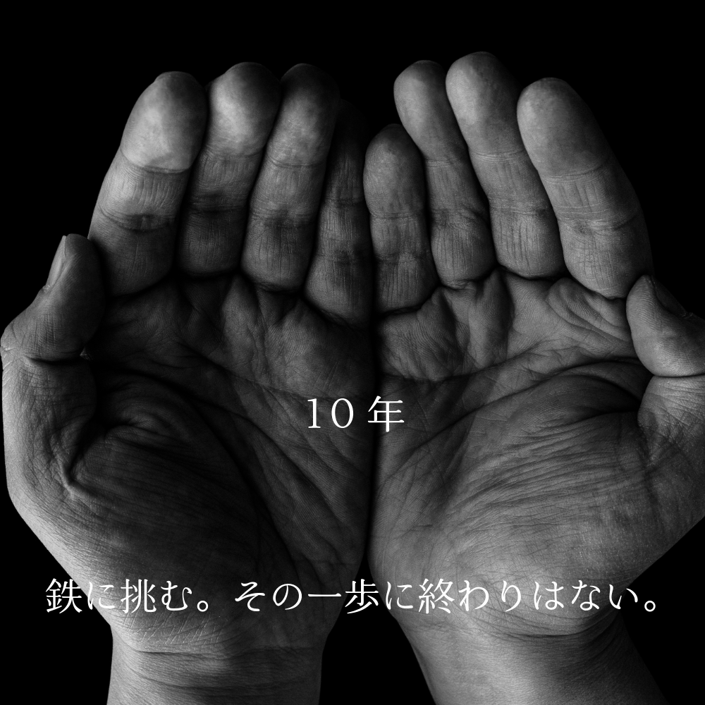 黒い背景に重ねられた職人の両手のモノクロ写真。中央に「10年」、下部に「鉄を拒む。その一歩に終わりはない。」という文字が重なっている。
