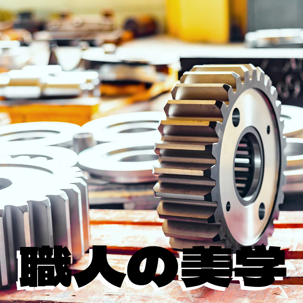 alt="工場内に並べられた精密な金属製の歯車（ギア）のアップ写真。手前に『職人の美学』の黒い文字"
